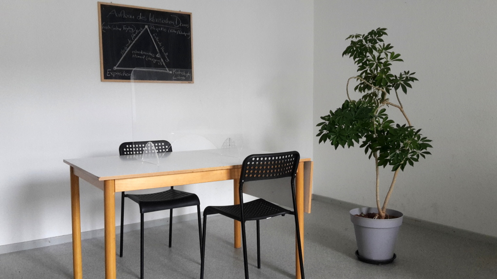 Raum für Einzelunterricht mit Spuckschutz am Platz und Tafel; Lehrbuchsammlung außerhalb des Bildes
